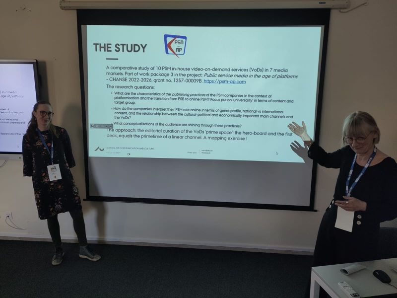 Photograph of a PSM-AP project's academic slide titled 'The Study' projected in a dimly lit room, with Hanne Bruun gesturing at the screen and Julie Mejse Munter Lassen standing to the side.